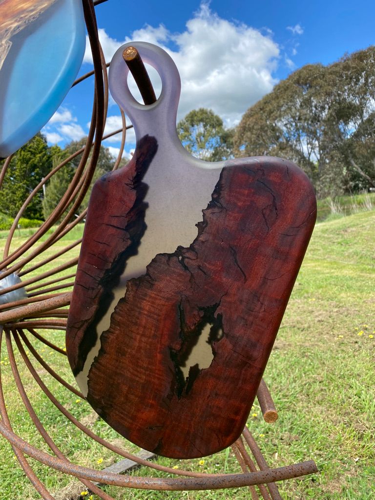 Wooden cutting board with dark red wood, light resin fill, and handle.