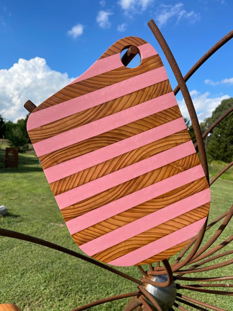 Pink and brown striped wooden sculpture against a blue sky, mounted on metal rods.