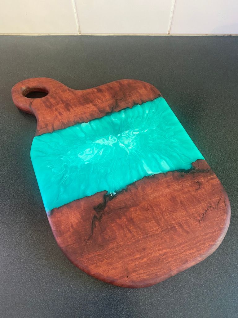 Wooden cutting board with teal resin center.
