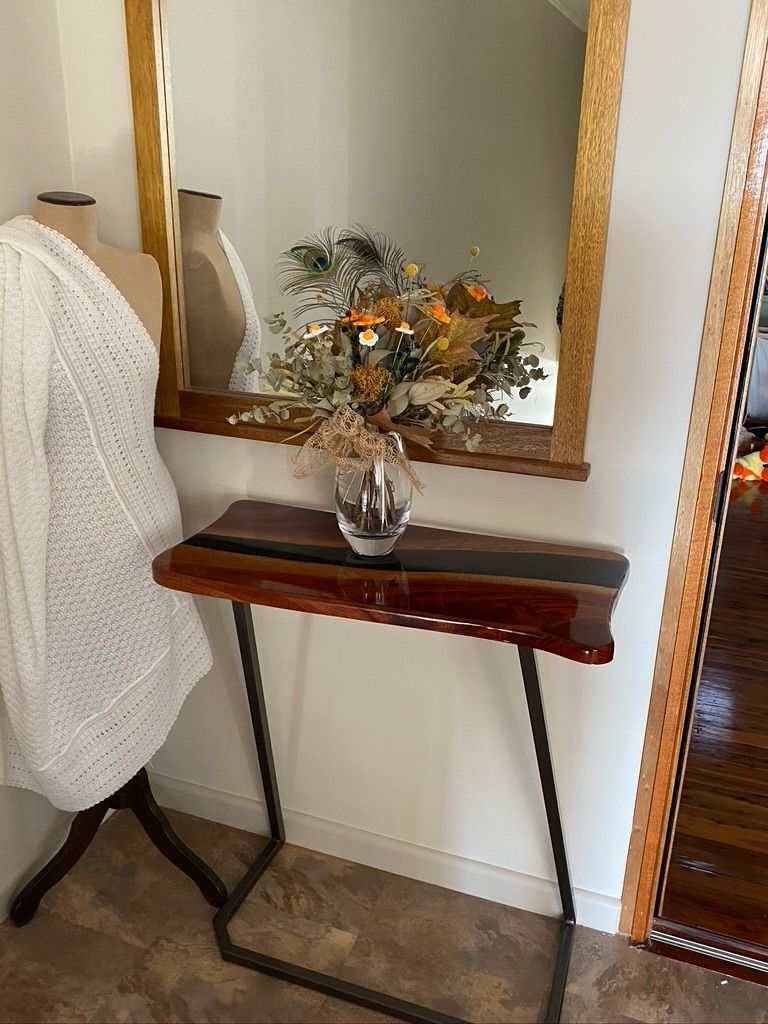 Wooden console table with floral arrangement beneath a mirror. A mannequin draped in a white sweater stands to the left.