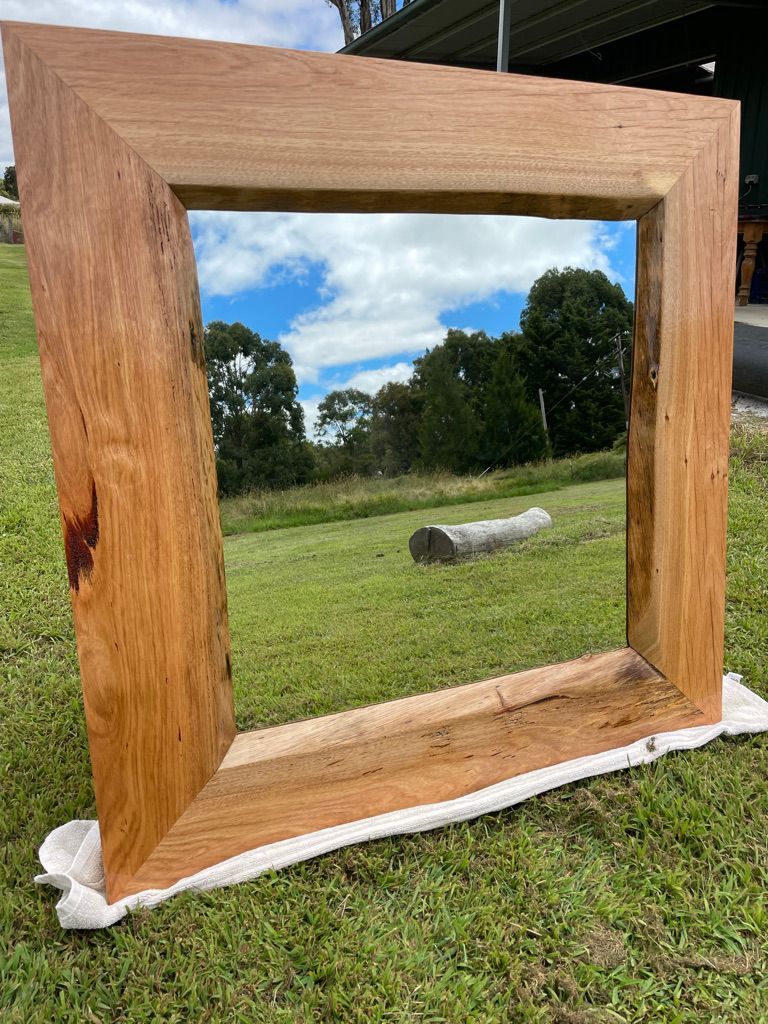 Large wooden-framed mirror outdoors, reflecting sky and trees.