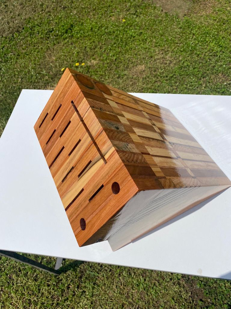 Wooden sculpture with diagonal layered design, brown hues, on a white table outdoors.