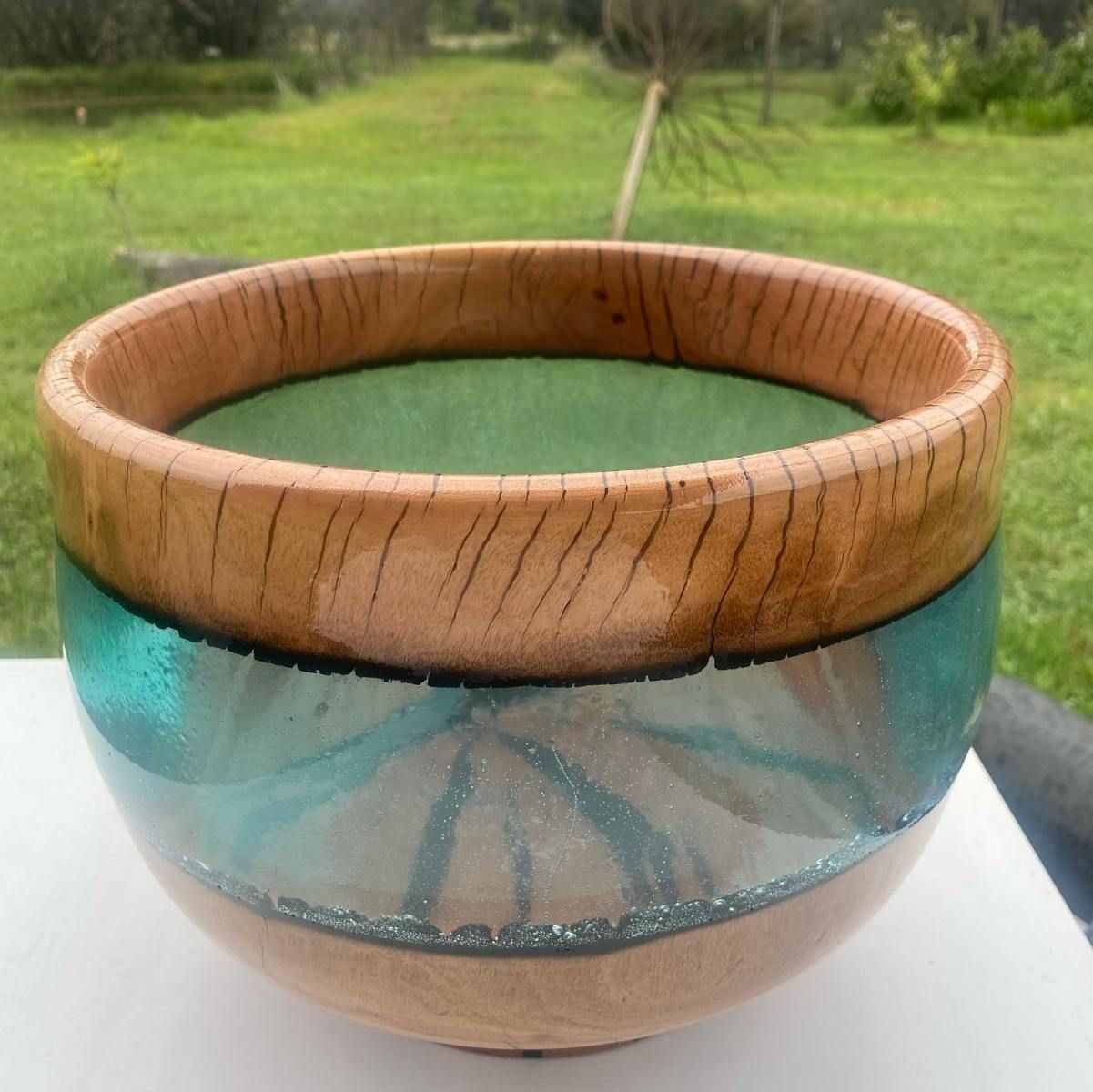 Wooden bowl with turquoise resin inlay. Bowl sits on white surface, with green grass in the background.