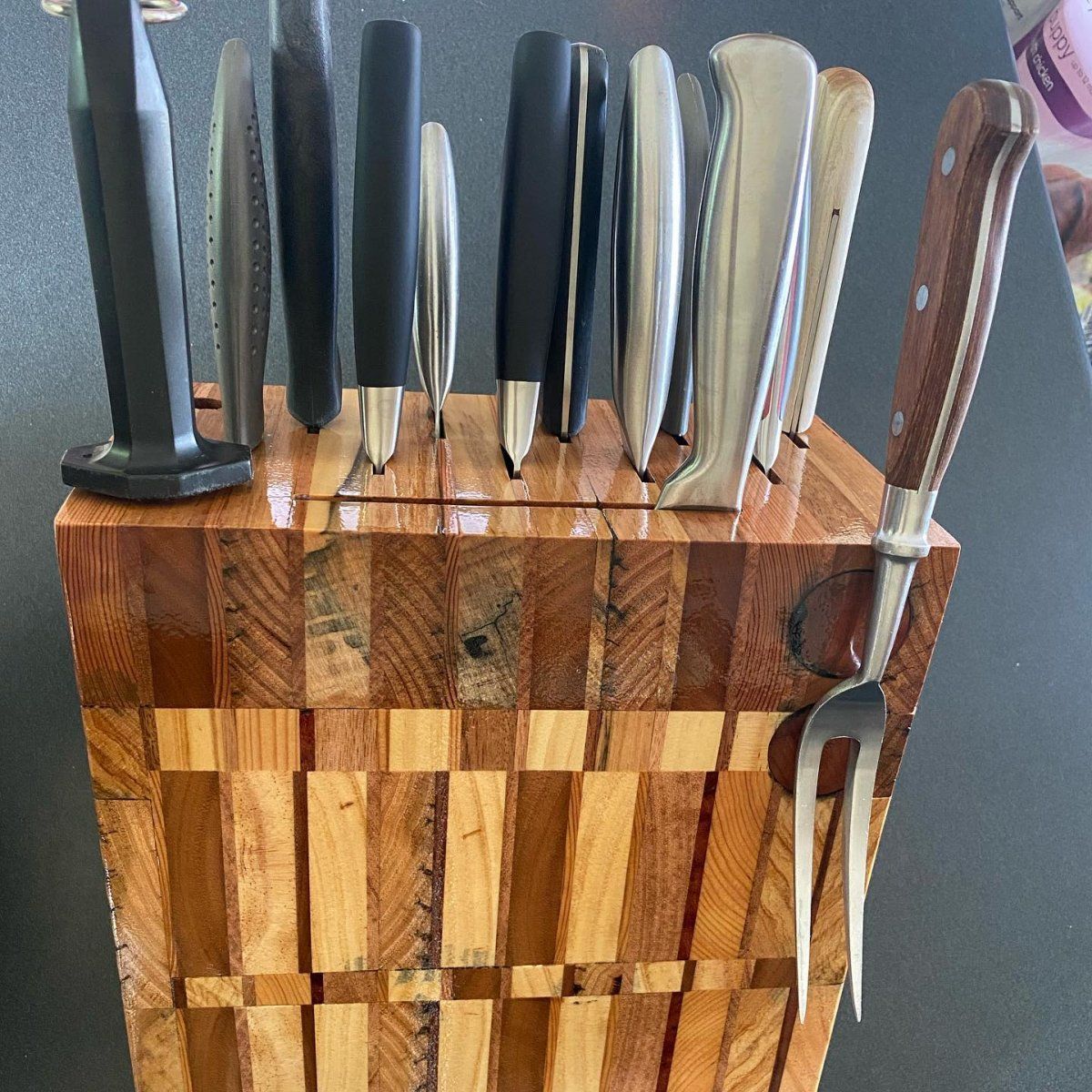 A wooden knife block holding various knives and a fork on a dark surface.
