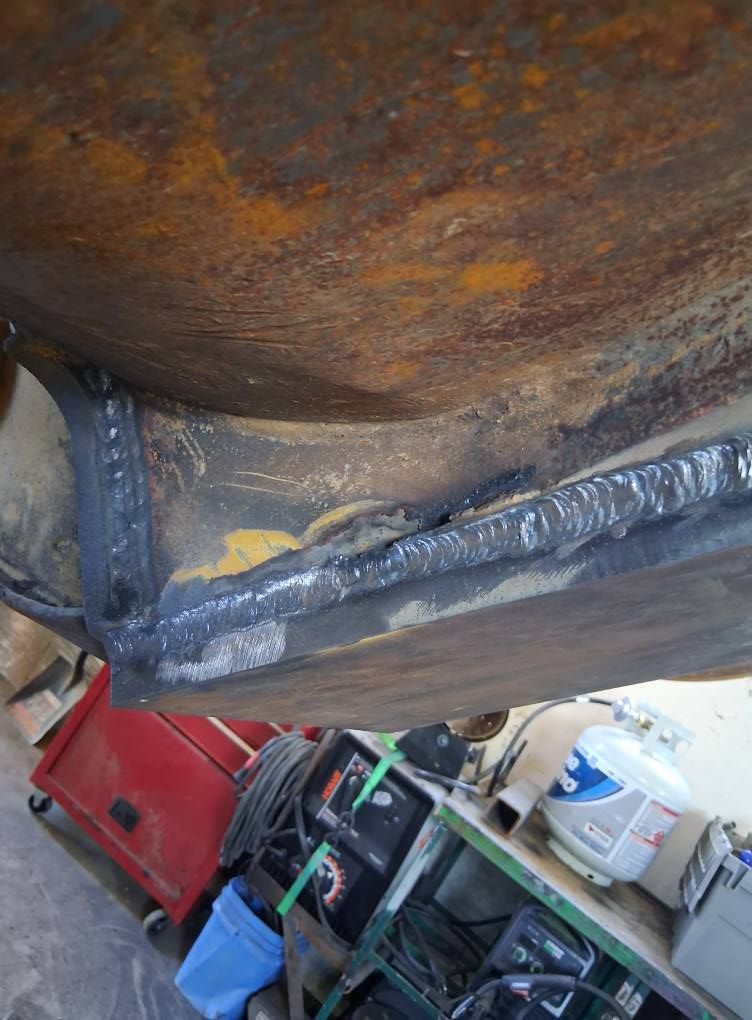 A close-up of a metal patch repair with fresh, thick welds joining two pieces of rusty industrial metal.