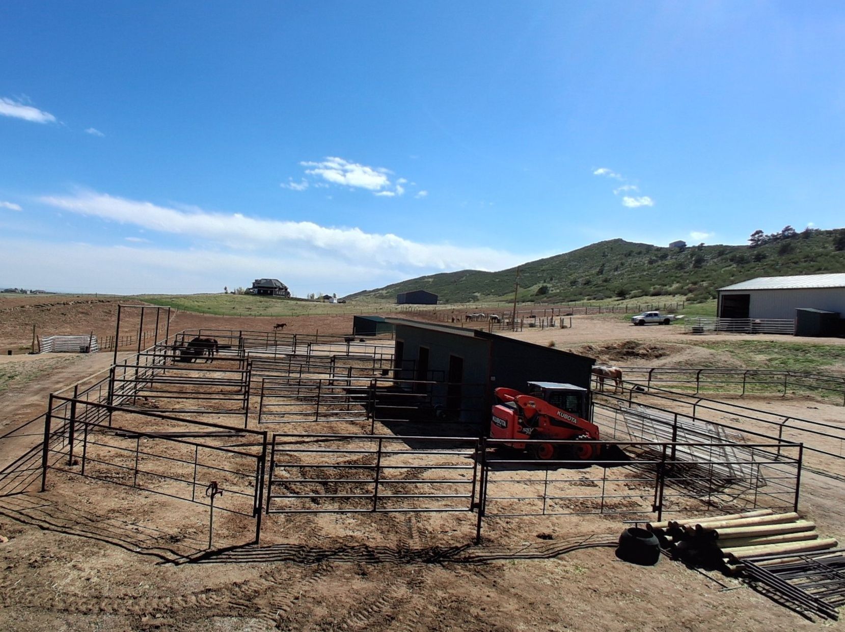 An outdoor construction site featuring a small, black rectangular structure surrounded by metal fencing and a red loader.