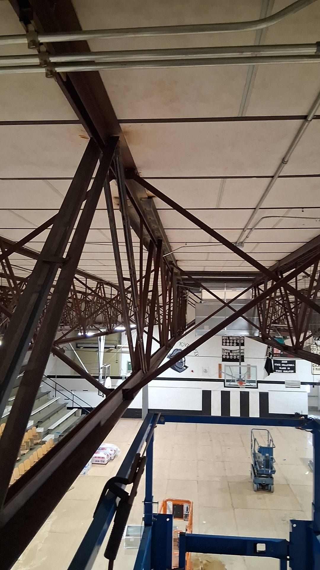 A view from a lift looking up at the metal trusses and ceiling of a high school gymnasium.