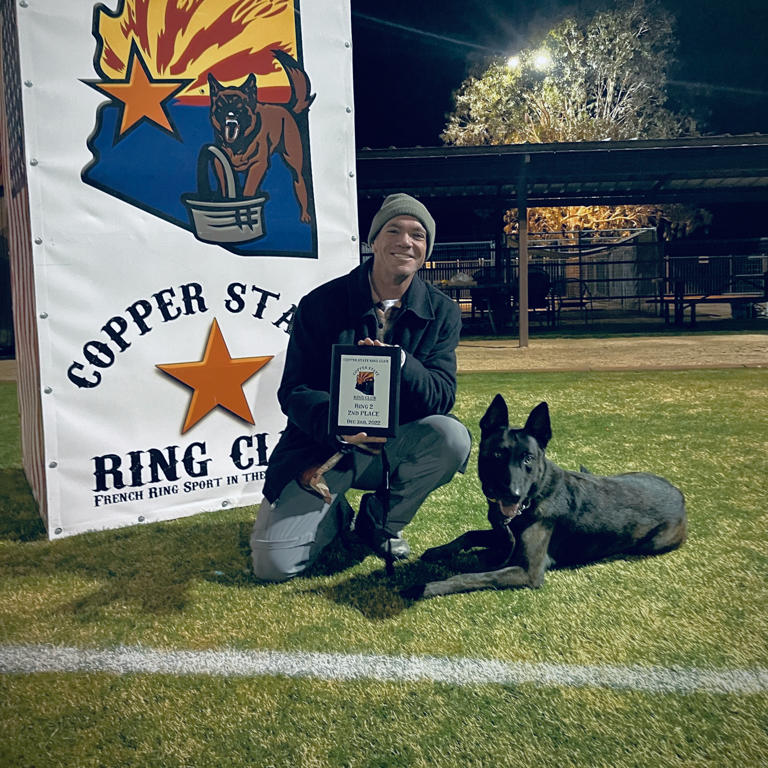 Chris Farr kneeling down next to a dog on a field holding a trophy.