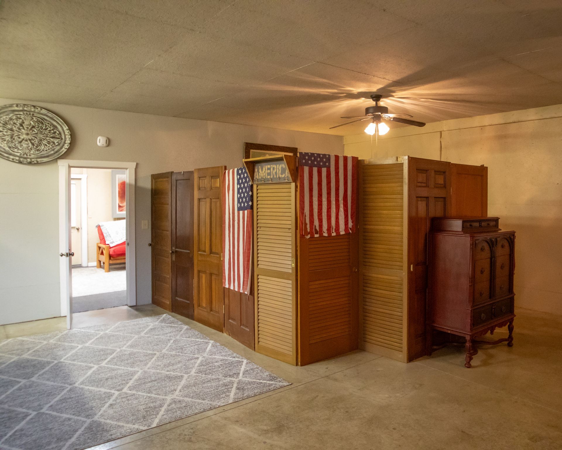 A room divider made of various wooden doors and screens, with American flags hung on it. A patterned rug is on the floor.