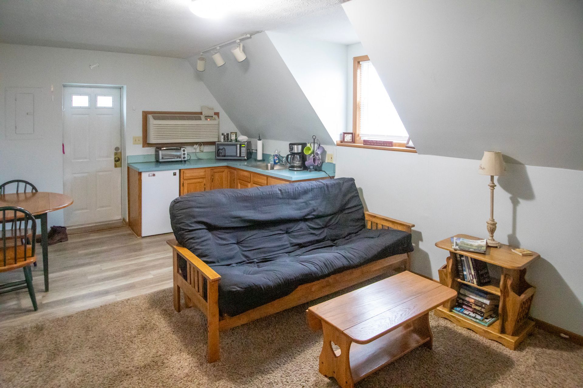 Cozy studio apartment with a futon, small kitchen, dining table, and sloped ceiling.