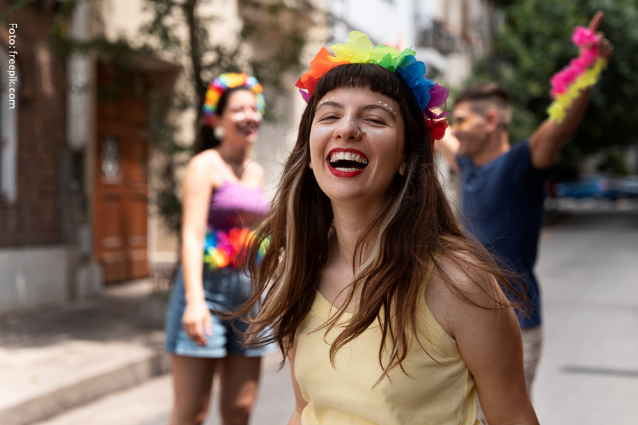 Pessoas comemoram, usando acessórios com as cores do arco-íris, em uma rua. Uma mulher ri, outras sorriem.