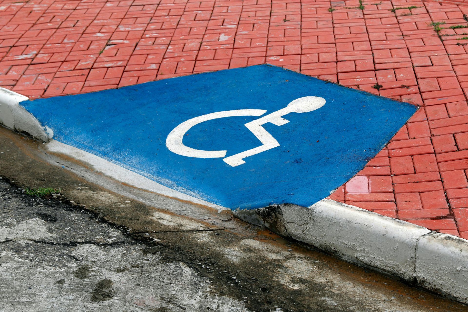Vaga de estacionamento para deficientes físicos pintada de azul em calçada de tijolos vermelhos.