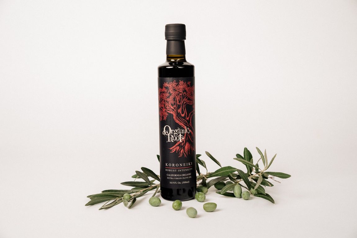 A bottle of olive oil is sitting next to a bunch of olives.