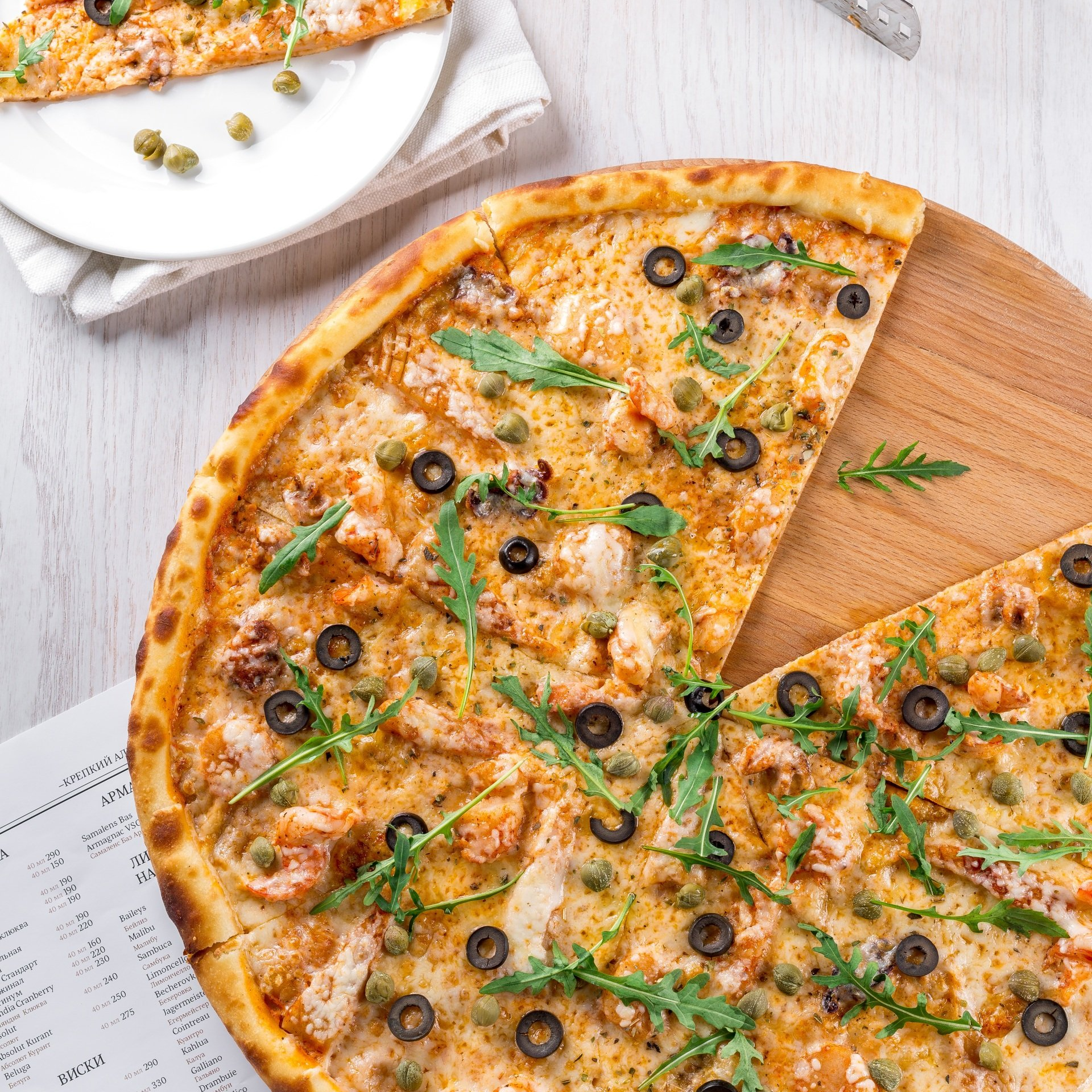A pizza with a slice taken out of it is on a wooden cutting board.