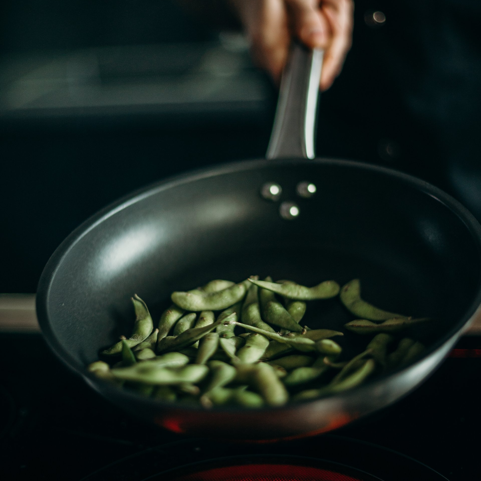 A person is cooking green beans in a frying pan on a stove.
