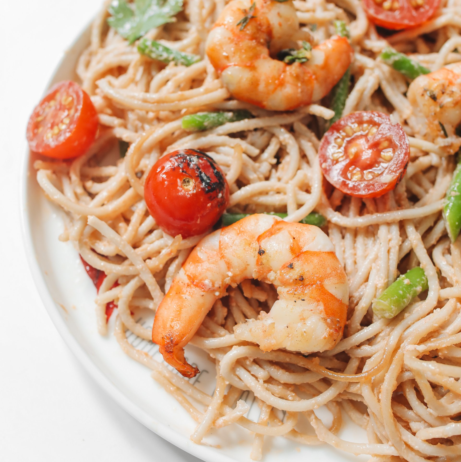 A white plate topped with noodles , shrimp , tomatoes and green beans.