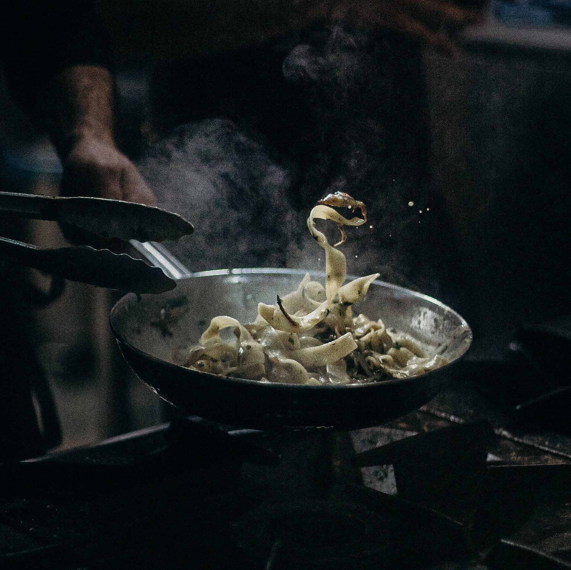A person is cooking noodles in a frying pan on a stove