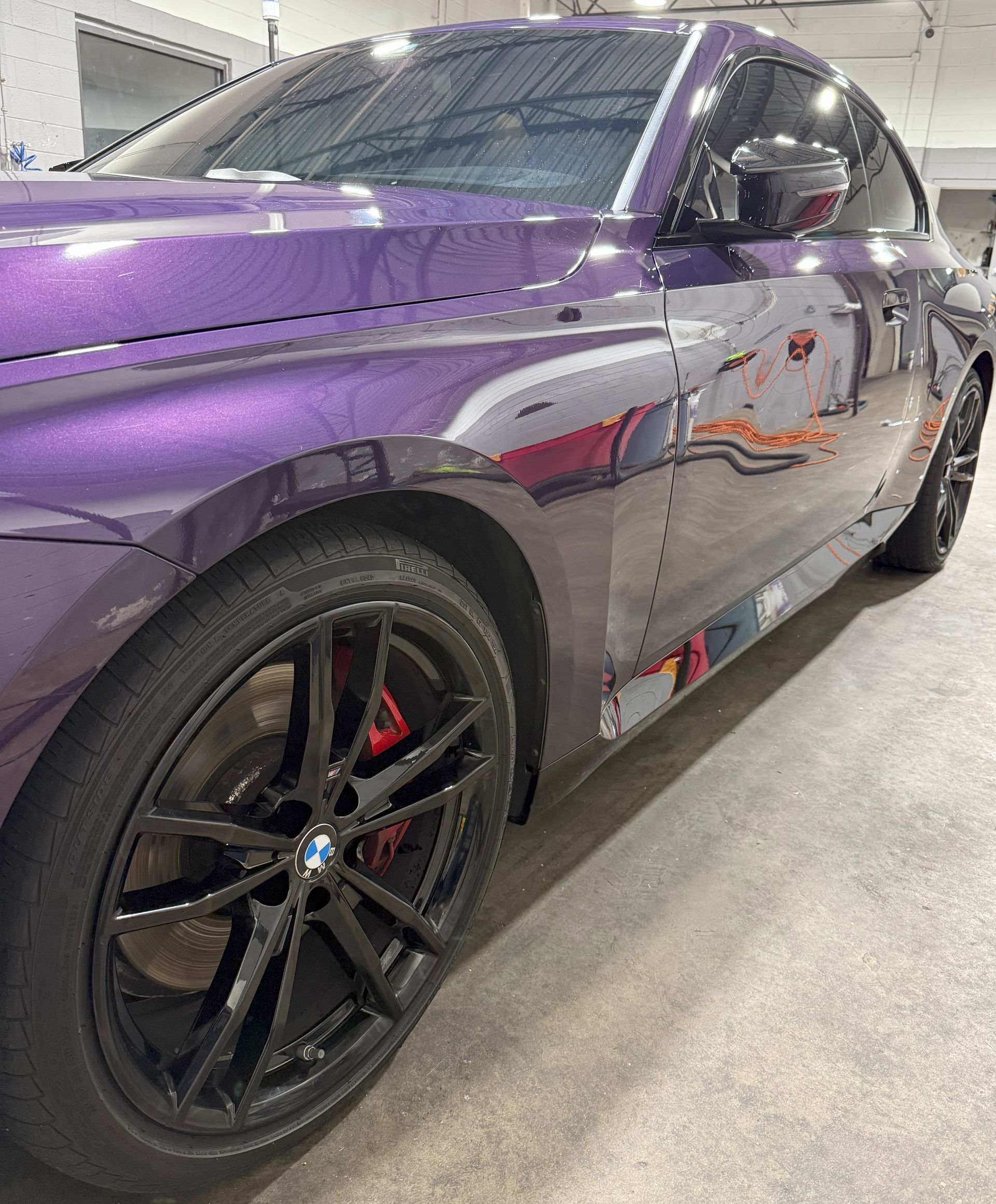 Purple BMW coupe with black rims and red brake calipers, parked inside.