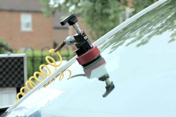 Windshield crack repair tool attached to a car windshield; outdoors, a residential setting.