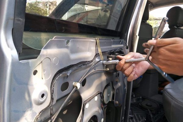 Person using a wrench to repair the inside of a car door. Silver metal, dark interior.