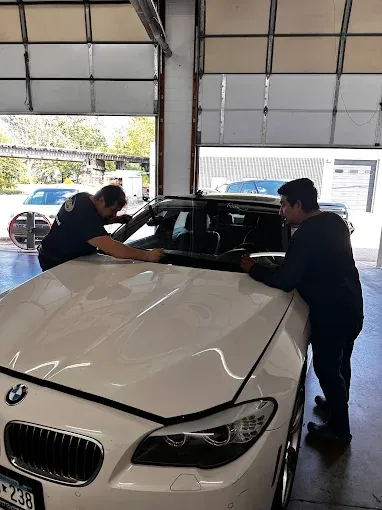 Two men installing a windshield on a white BMW inside a garage.