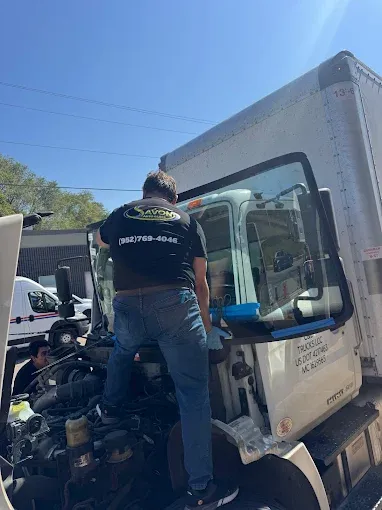 Man replacing windshield on a white box truck, outdoors on a sunny day.