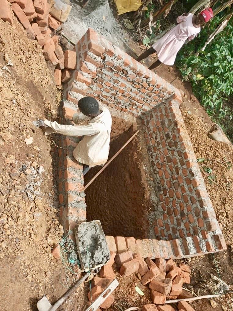 Man bricklaying inside a brick structure, two children watch from above.