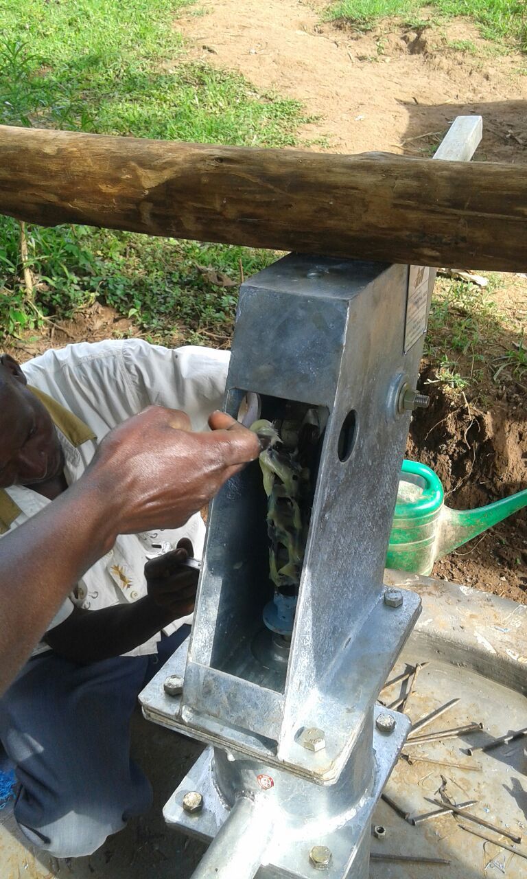 Man working on a water pump, removing material with his hand. Pump is metal and sits outside.