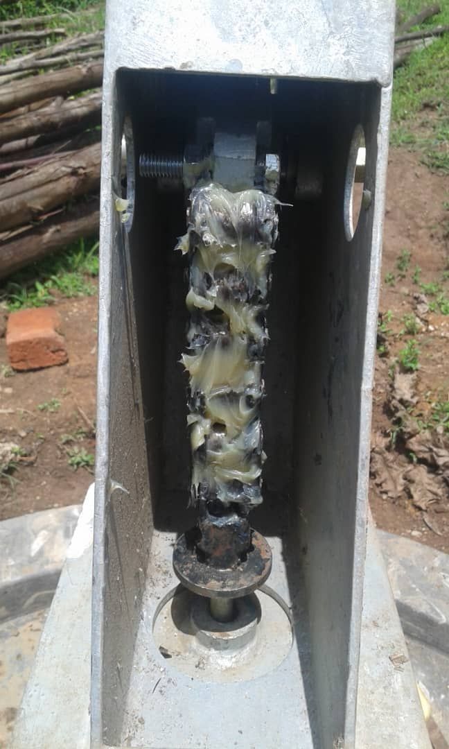 Greased metal rod within a gray metal frame, likely part of machinery, outdoors.