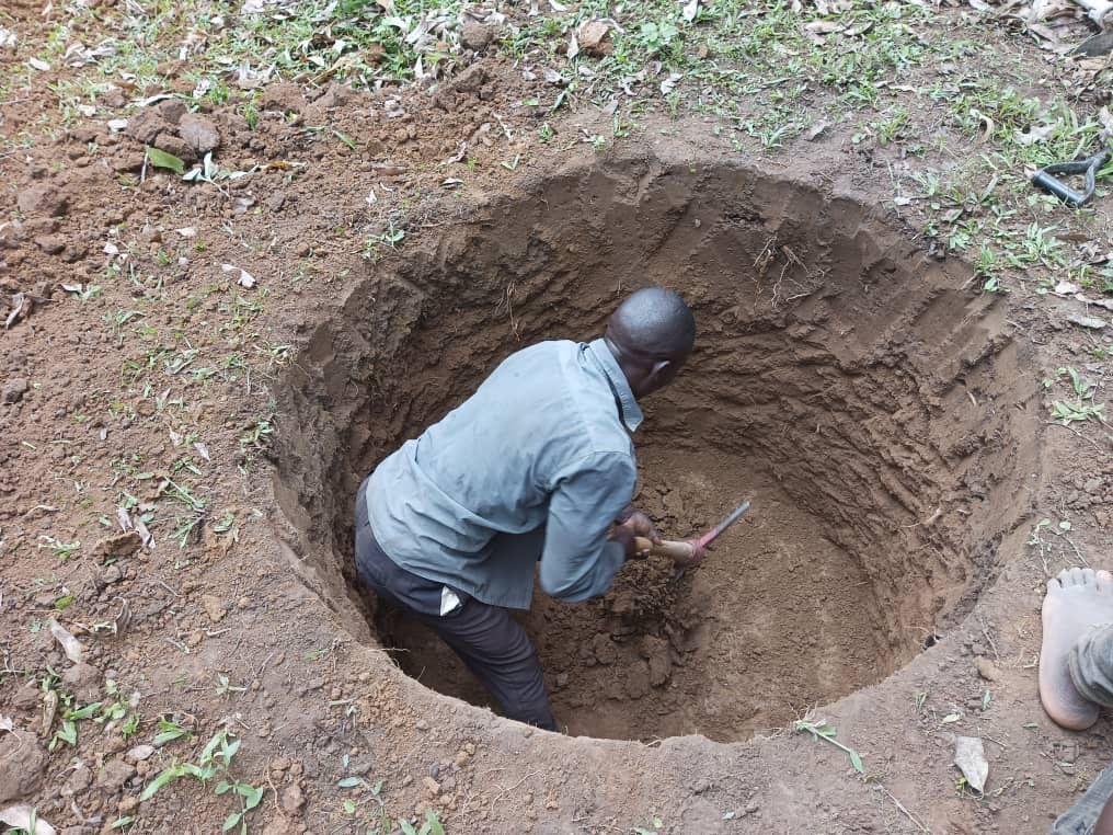Man inside a large dirt pit, using a small tool to dig.