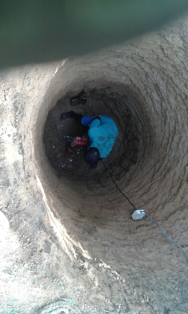 Person in a well, wearing blue and red, looking up. The well is circular, made of brown earth.