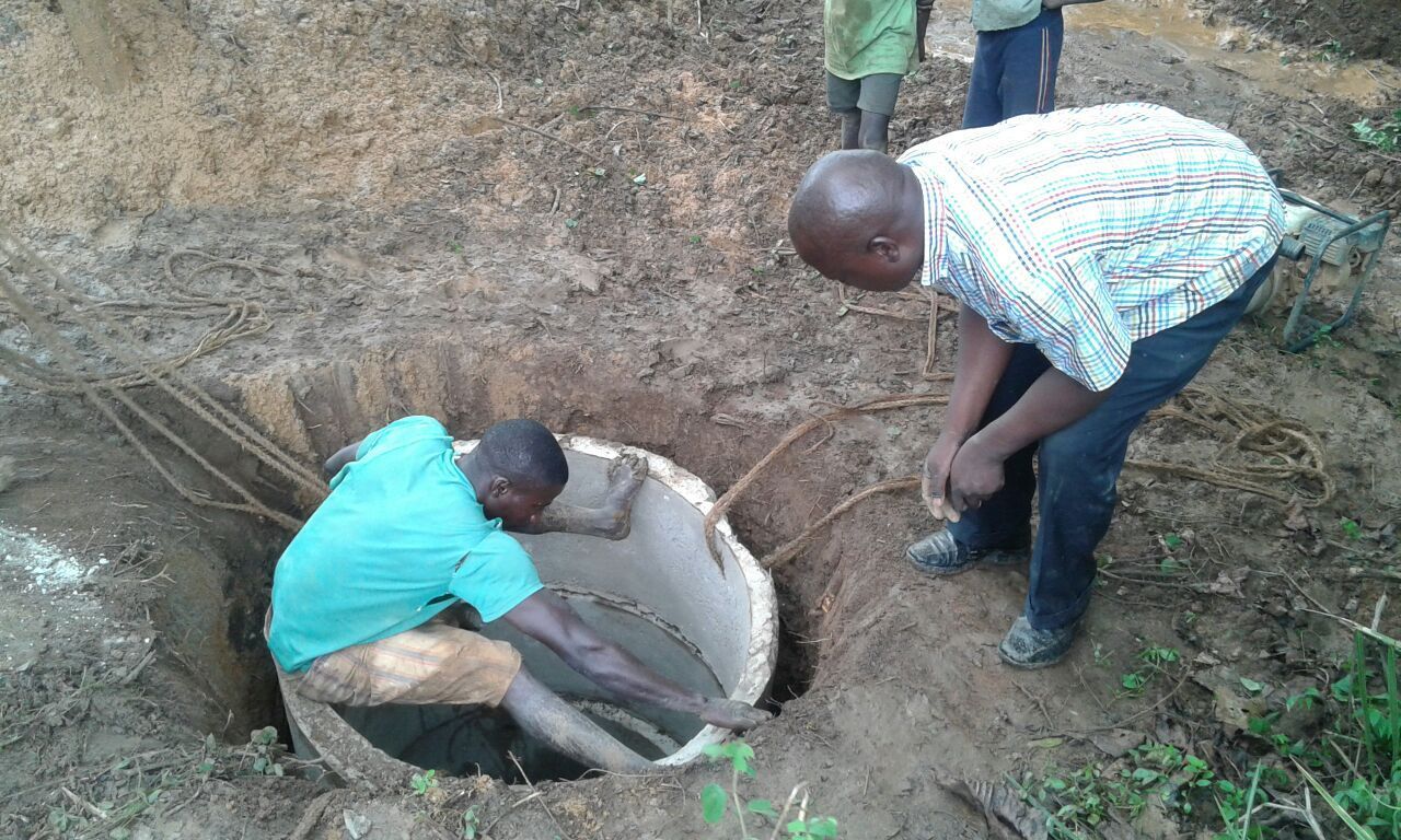 Two men in dirt hole inspecting a circular, stone-like object, possibly a well or vault.