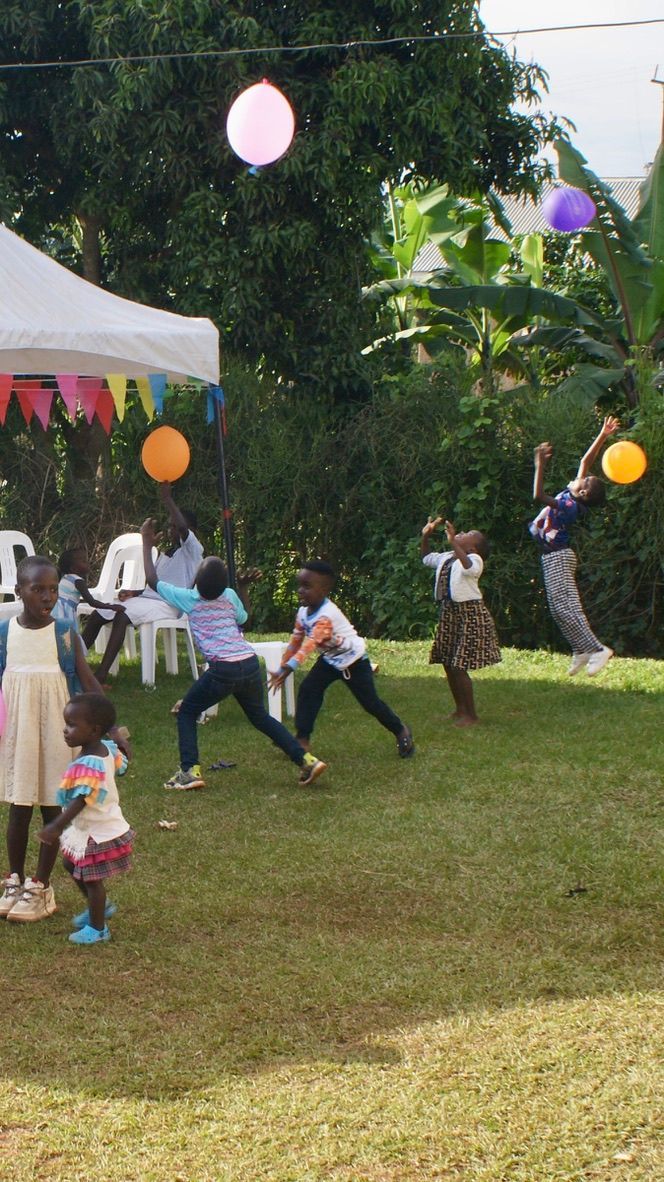 Children playing in a yard with balloons. Party tent and decorations in the background.