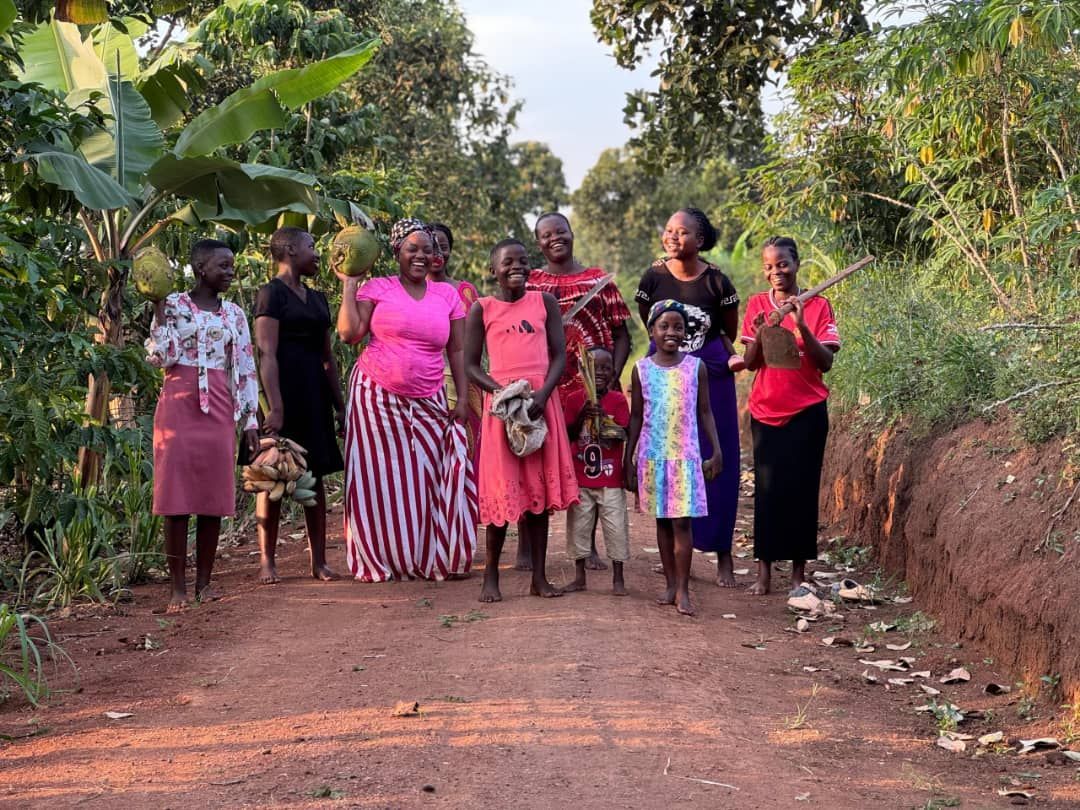 Group of people standing on a dirt road, trees on both sides. They are smiling.