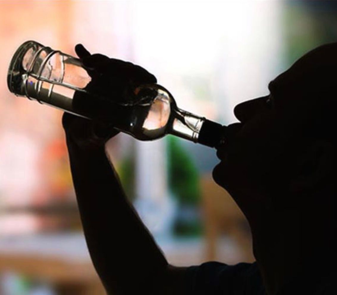 Silhouette of a person drinking directly from a clear glass bottle.