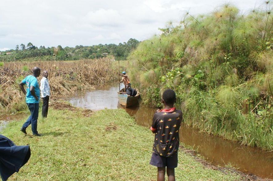 People standing near a narrow waterway with a boat.  Green vegetation lines the banks.