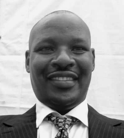 Man in suit smiles at camera, wearing tie, against a white backdrop.