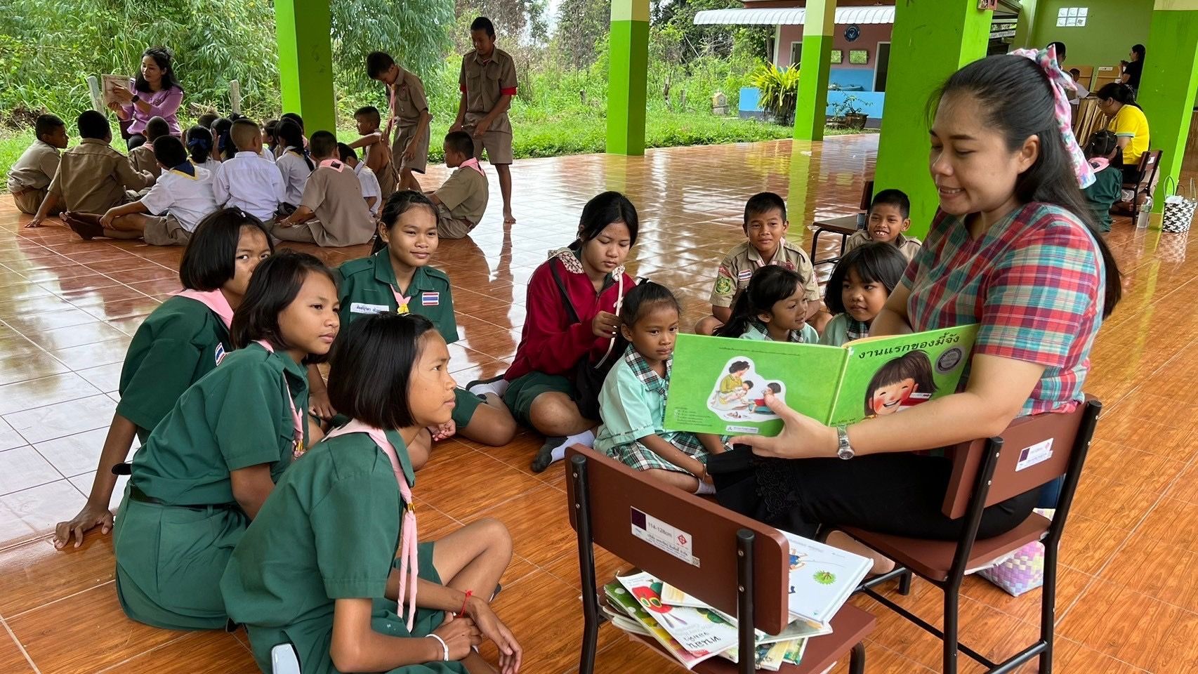 Teacher reading a book to a group of children, outdoors.