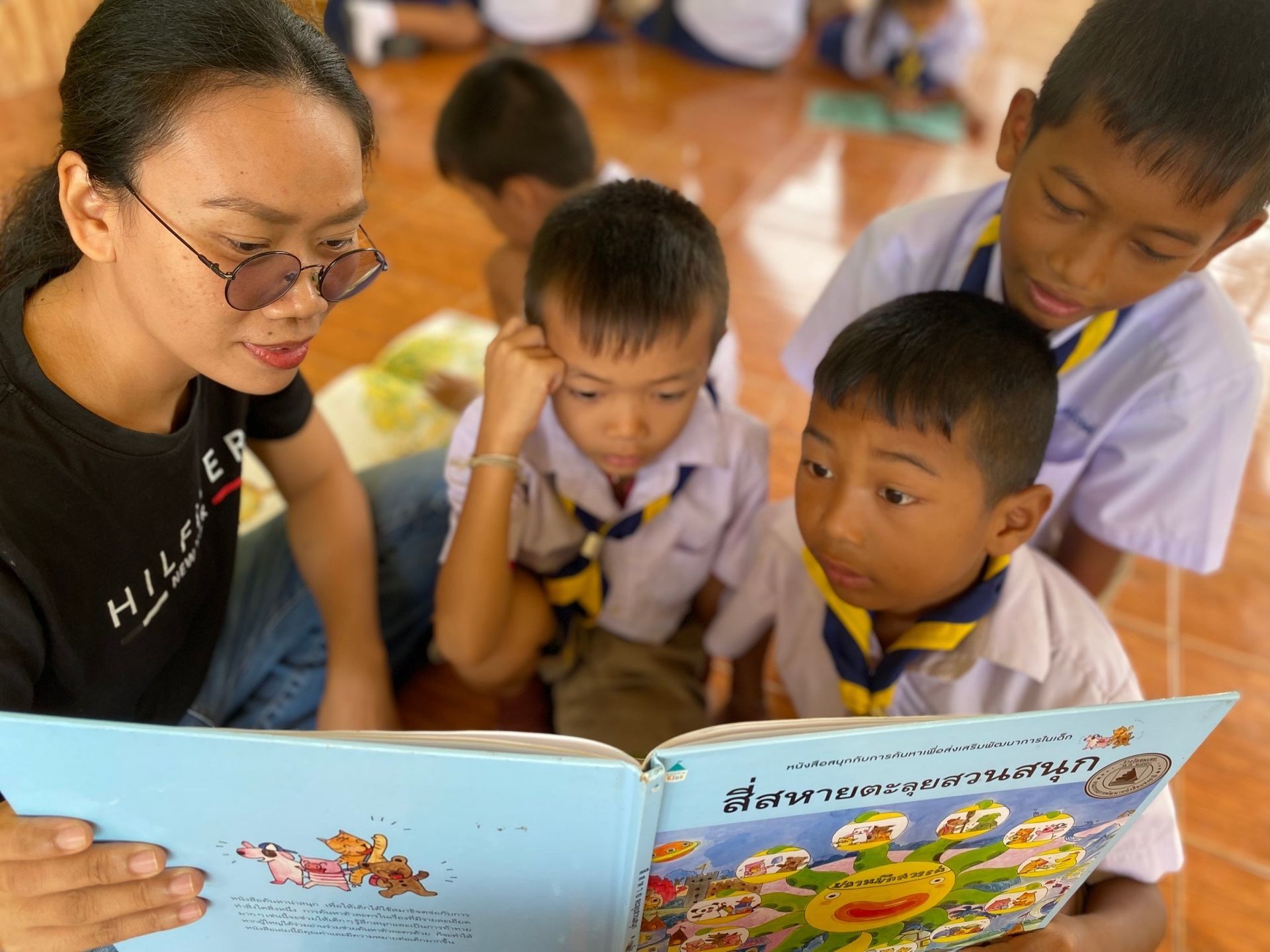 Woman reading a picture book to three children in school uniforms.