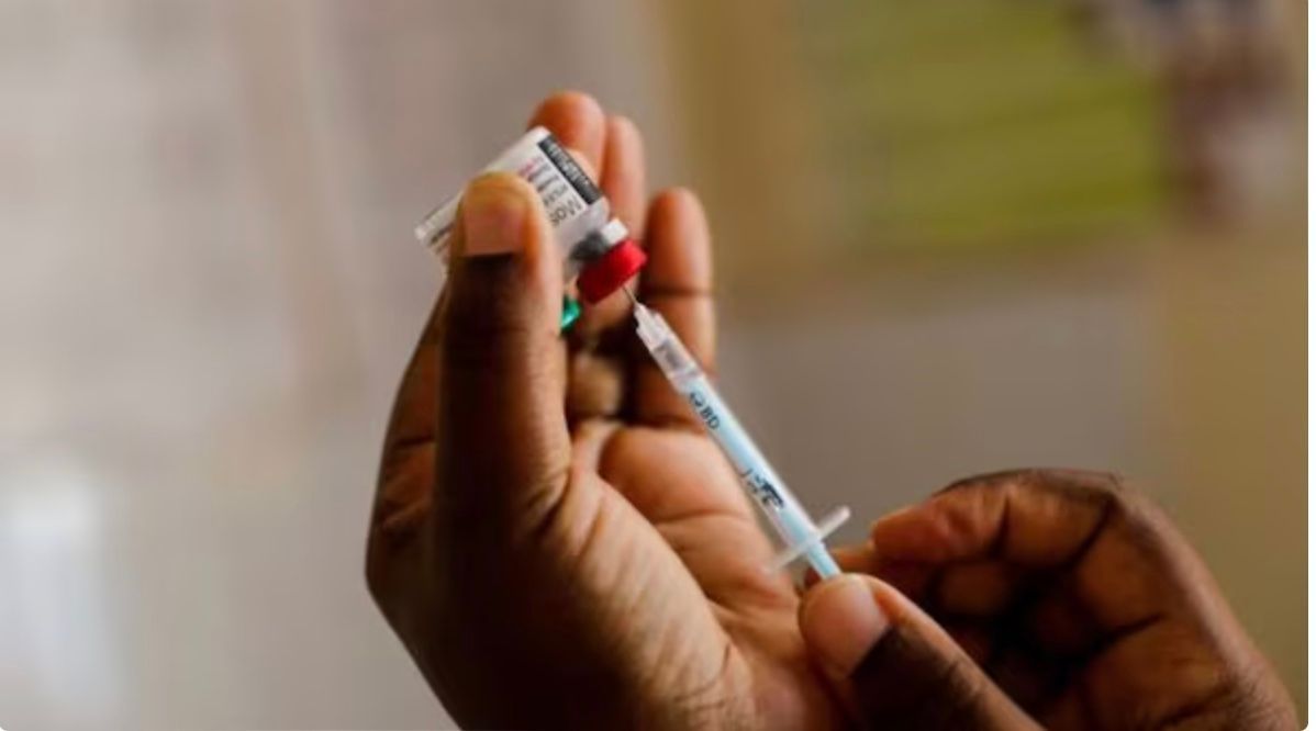 Person filling syringe from a vial. Syringe and vial are held in hand with red and white cap.