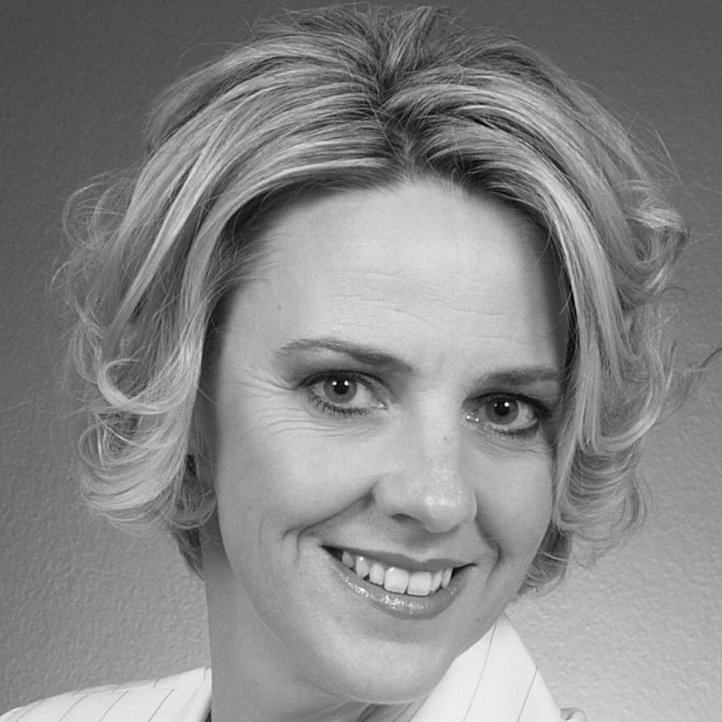 Woman with blonde hair smiling, wearing a white collared shirt, headshot.