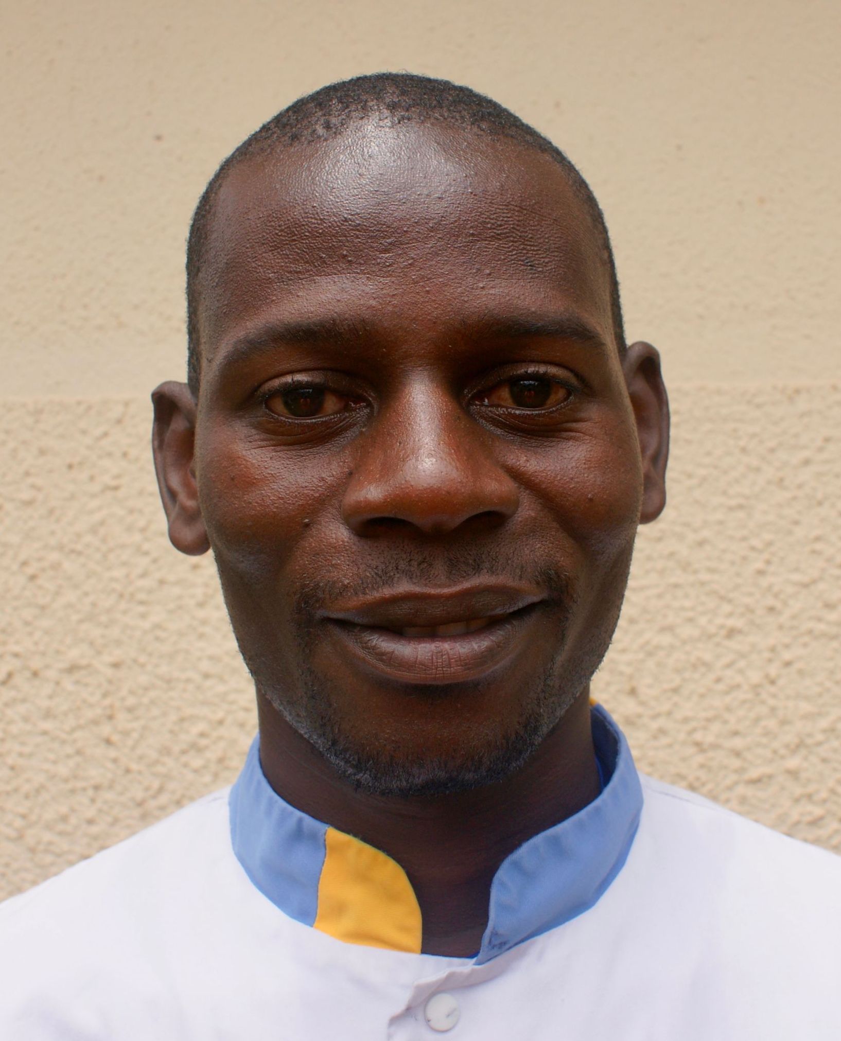 Man wearing a white shirt with blue and yellow collar smiling at the camera, neutral background.