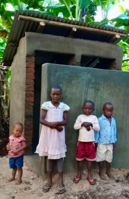 Four children stand in front of a concrete building with a tin roof.