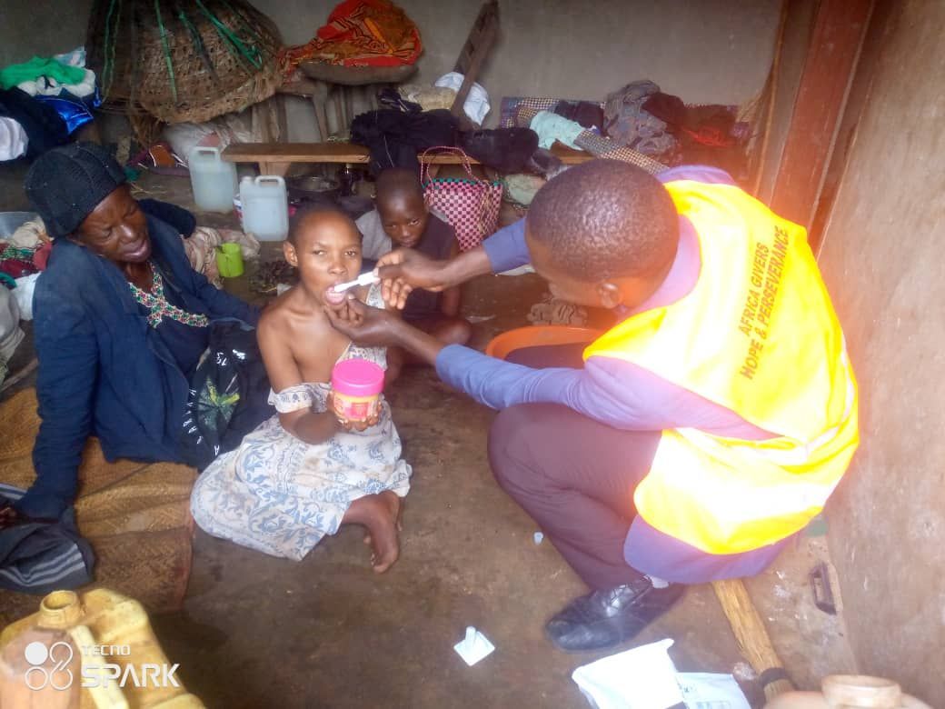 A healthcare worker gives medication to a child indoors, watched by a woman and another child.