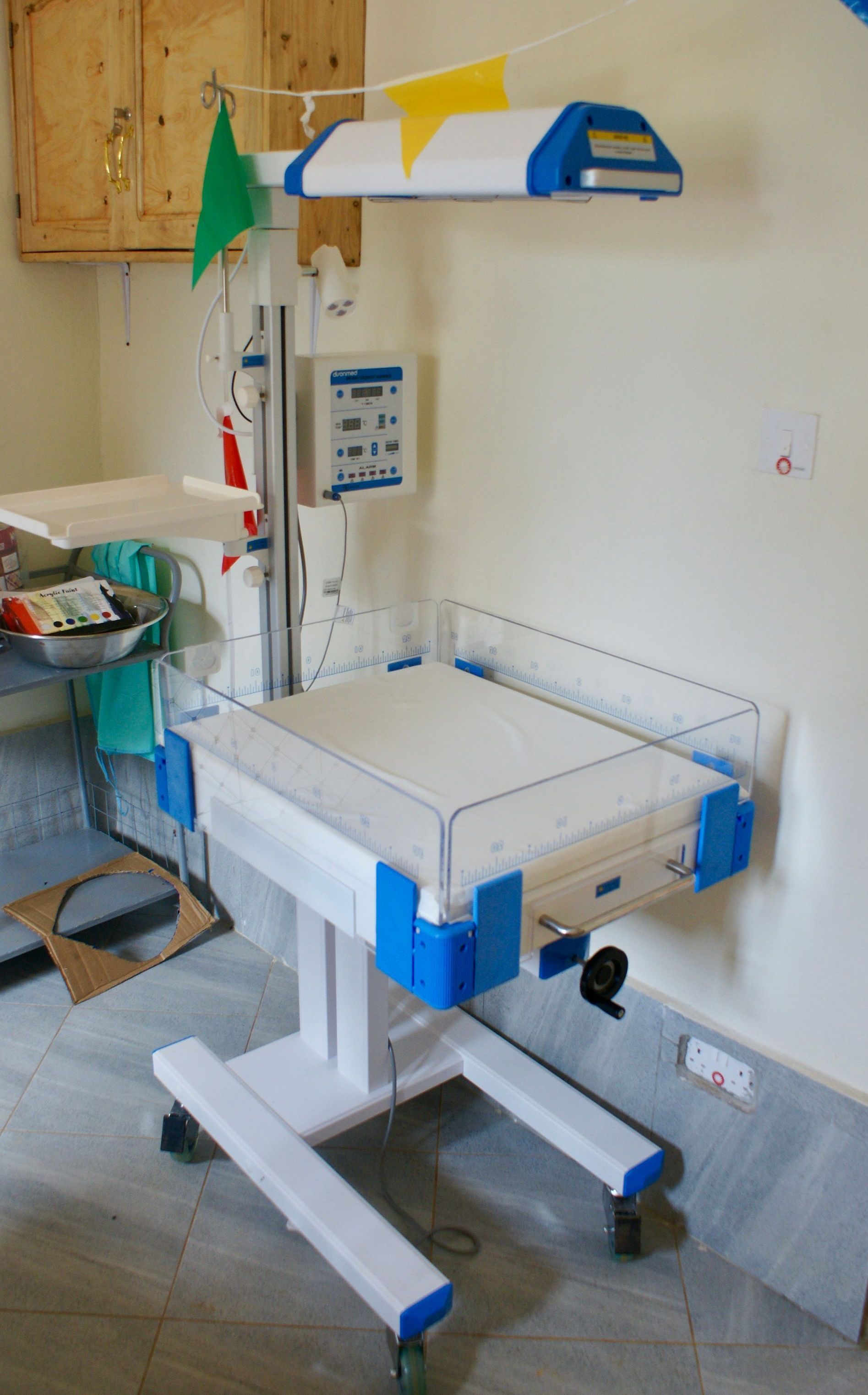 An infant radiant warmer in a medical setting, white and blue, with a control panel and lights.