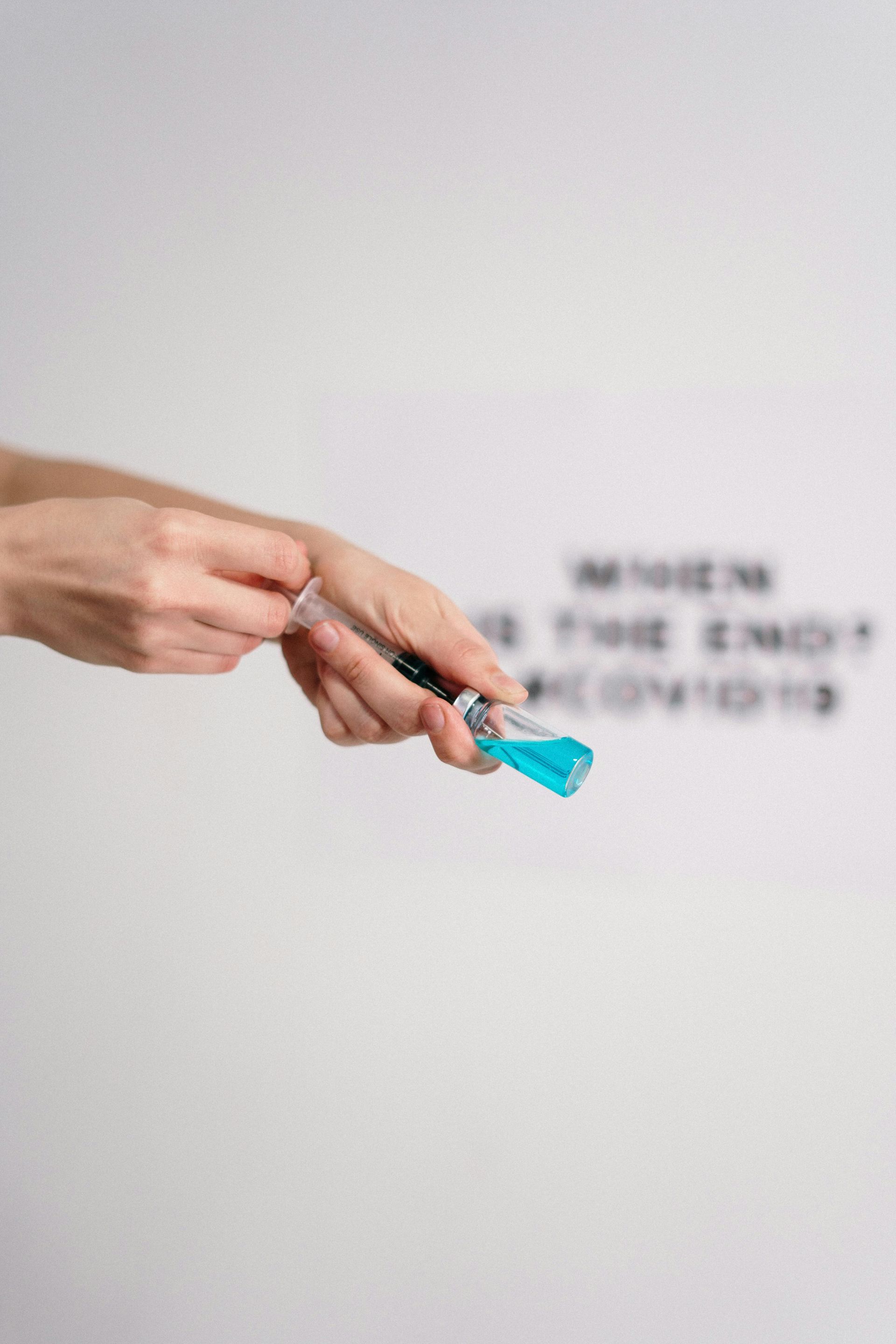 Hands preparing a syringe for injection; white background with blurred text.