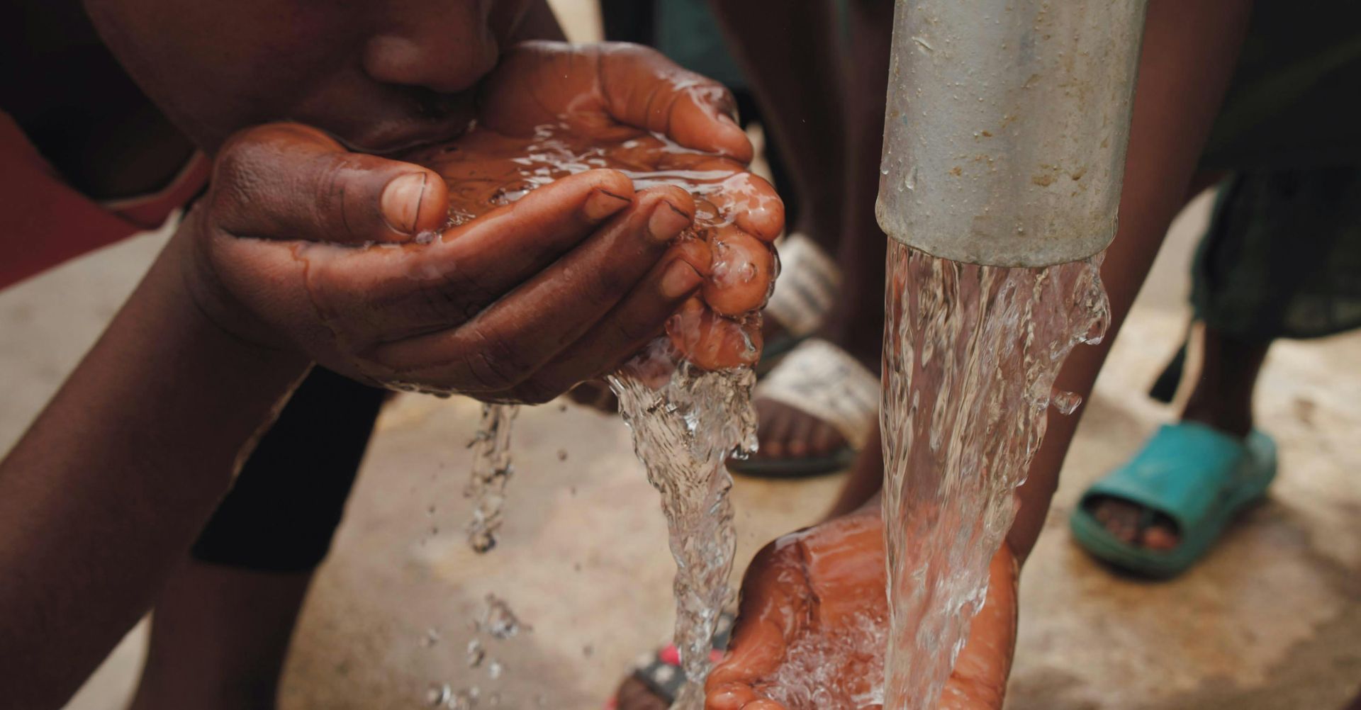 Hands cupped under a flowing water faucet, collecting water to drink.