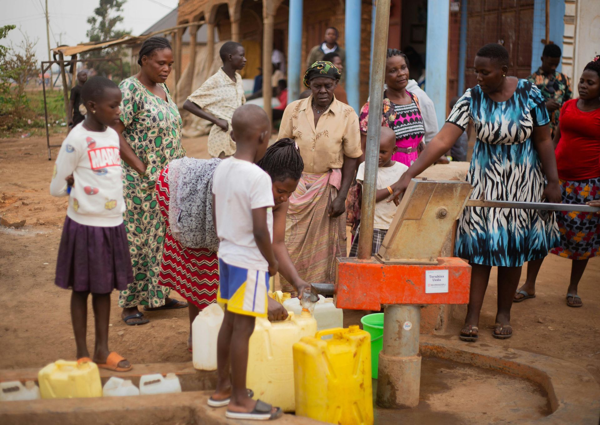 People collecting water from a pump in a rural setting; children and adults fill jugs.