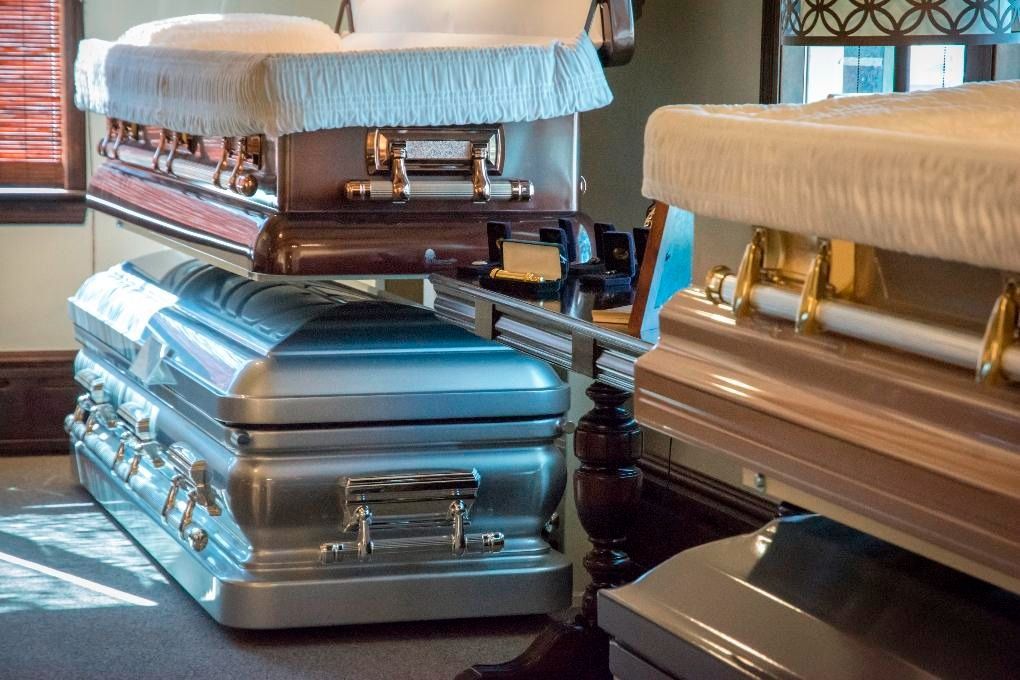 Two closed caskets in a funeral home, one silver and one white with gold accents
