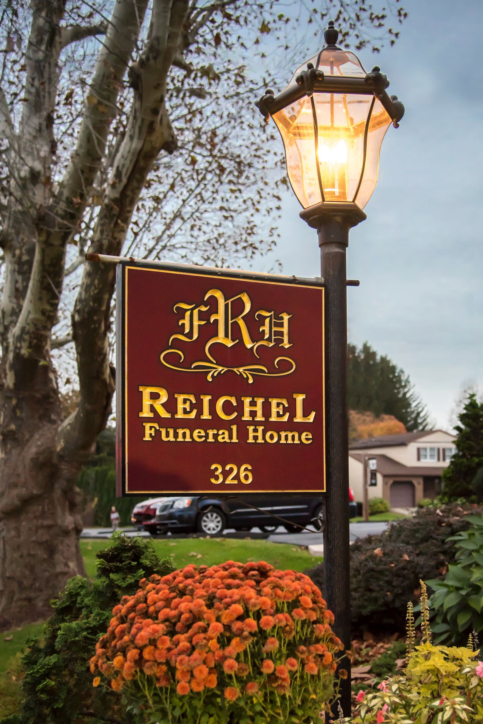 Lit lamppost beside Reichle Funeral Home sign and orange flowers outside